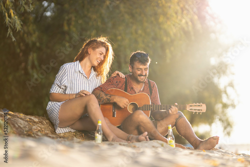 couple sitting on the beach and playing guitar © Nemanja