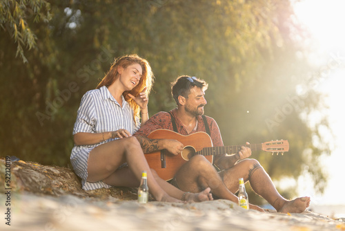 couple sitting on the shore and playing guitar