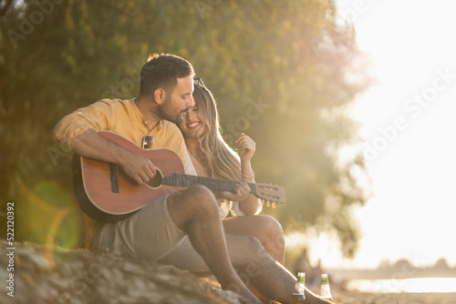 Man playing guitar with his girlfriend on beach side