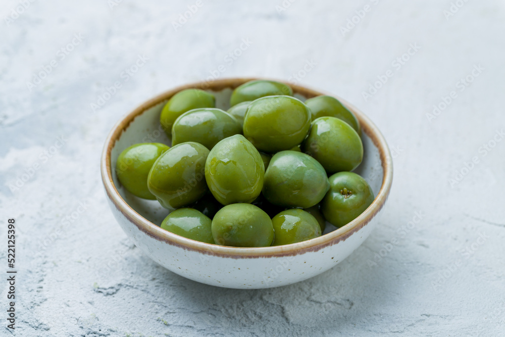 large green olives on bowl on white concrete table large green olives on bowl on white concrete table