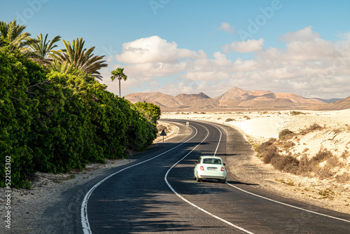 Helles Auto auf der FV-104 in den Dünen von Corralejo mit Palmen auf Fuerteventura