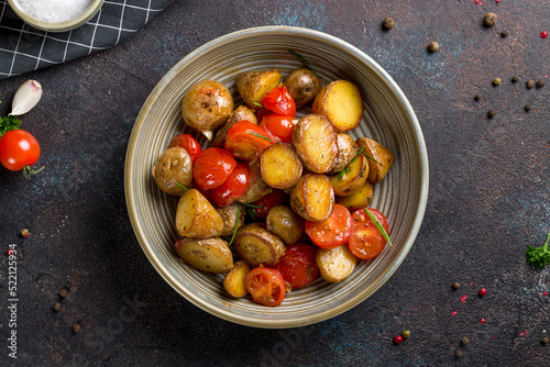 baked mini potatoes with tomatoes and rosemary top view on dark stone table