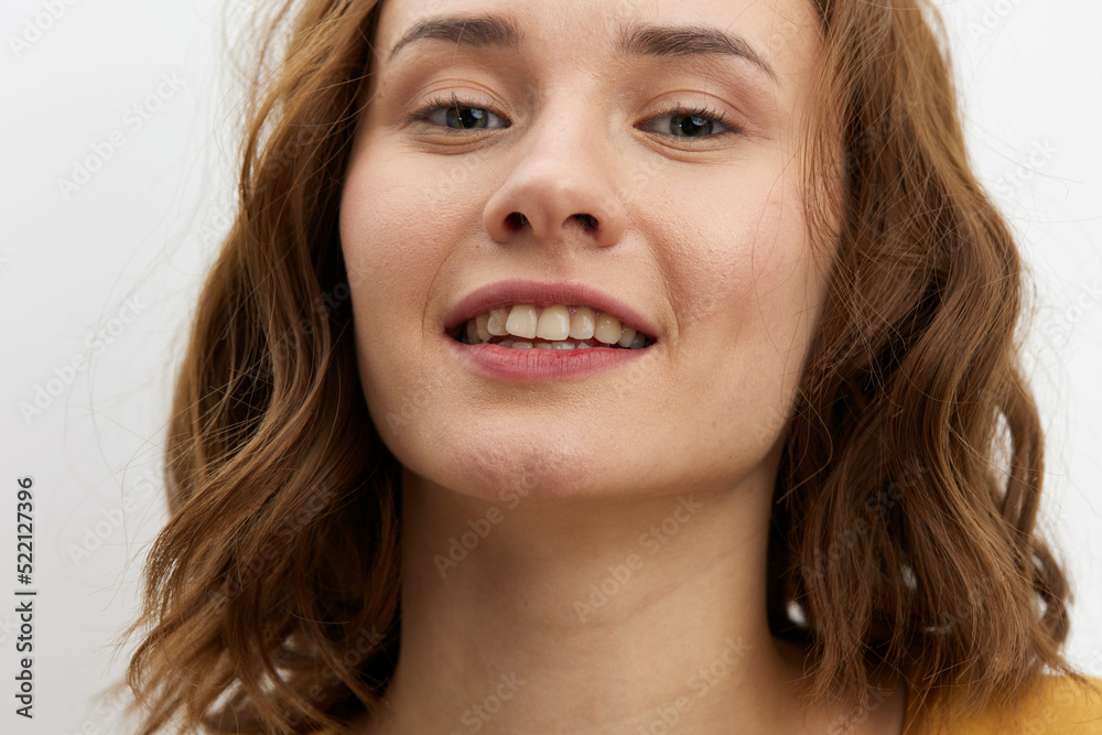 a close, horizontal portrait of a joyful, happy woman in a yellow T-shirt on a light background smiling broadly and looking at the camera a close, horizontal portrait of a joyful, happy woman in a yellow T-shirt on a light background smiling broadly and looking at the camera