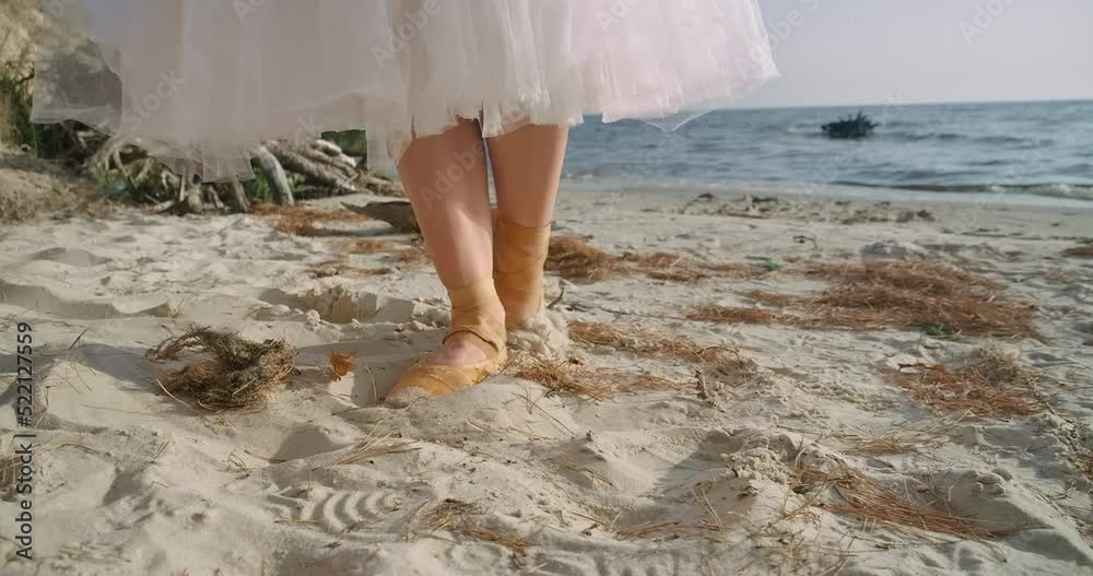Close-up steps of graceful talented ballet dancer in pointies on yellow sand at background of waves. Unrecognizable Caucasian confident woman walking in slow motion on beach. Cinema 4k ProRes HQ