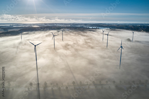 onshore wind turbine standing in fog in the morning sun