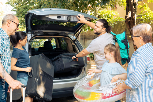 Big european family going on holiday vacation and loading baggage in automobile trunk. Child travelling with parents and grandparents at seaside during summer, putting luggage in vehicle.