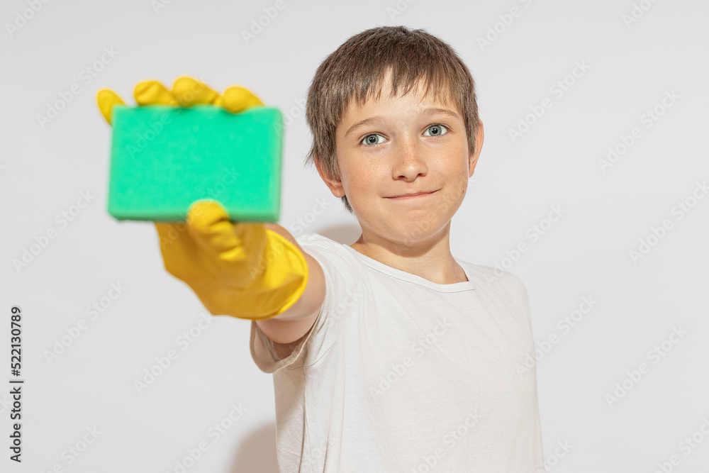 A smiling teenager, in rubber yellow gloves, holds out a sponge for washing into the camera. The concept of cleaning and cleanliness. A smiling teenager, in rubber yellow gloves, holds out a sponge for washing into the camera. The concept of cleaning and cleanliness.