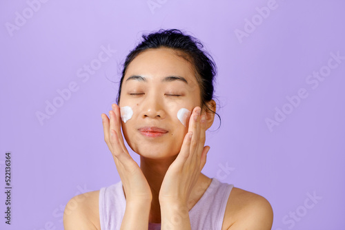 Female model putting cream on her glowing face skin.