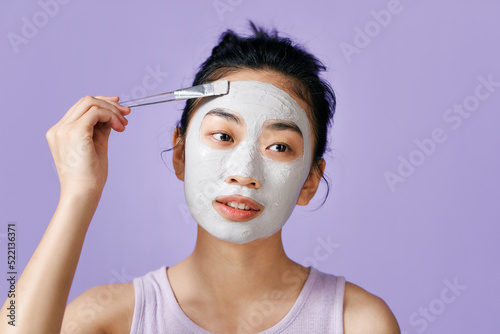 Young woman applying gray-blue face mask - studio portrait