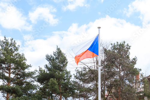 Czech flag on a background of blue sky and green trees.