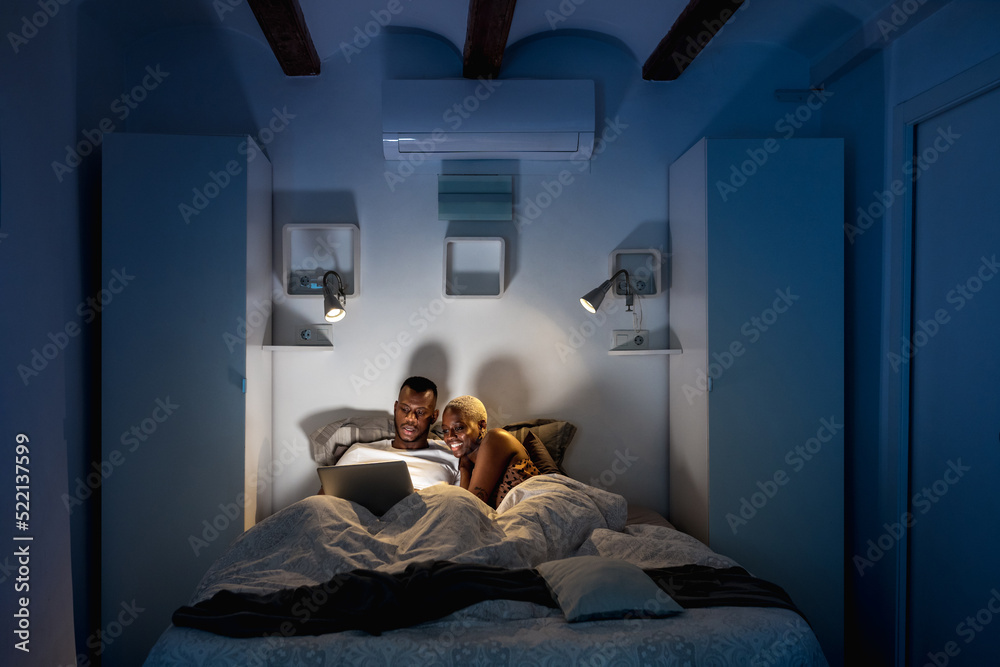 © Ezequiel Giménez/Stocksy - Black couple watching video before sleep