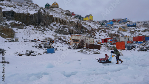 Northern Greenland coastal settlement inhabitant pushes girl on sled
