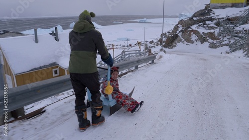 Dad pushes young daughter down a snowy road sitting on sleigh photo