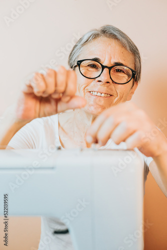 Old woman tailor preparing a sewing machine sews reuses fabric from old denim clothes. Re-use old fabrics for new clothes, sustainability. Old people new hobby at home, seniors mental activity and job photo