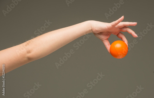 female hands holding an orange sponge ball on a gray background isolated