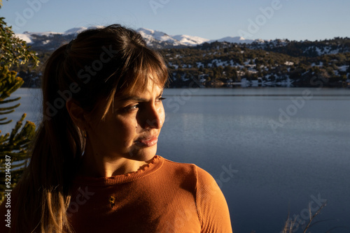 Portrait of a young woman looking at the beautiful landscape, at sunset. The blue lake, forest and mountains in the background.