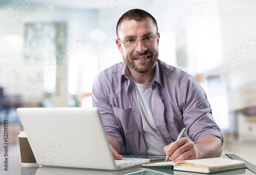 Happy satisfied millennial man using laptop at office workplace, working, thinking, watching online webinar, training, making payment