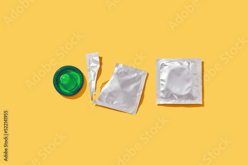 Opened and sealed condoms on yellow background.