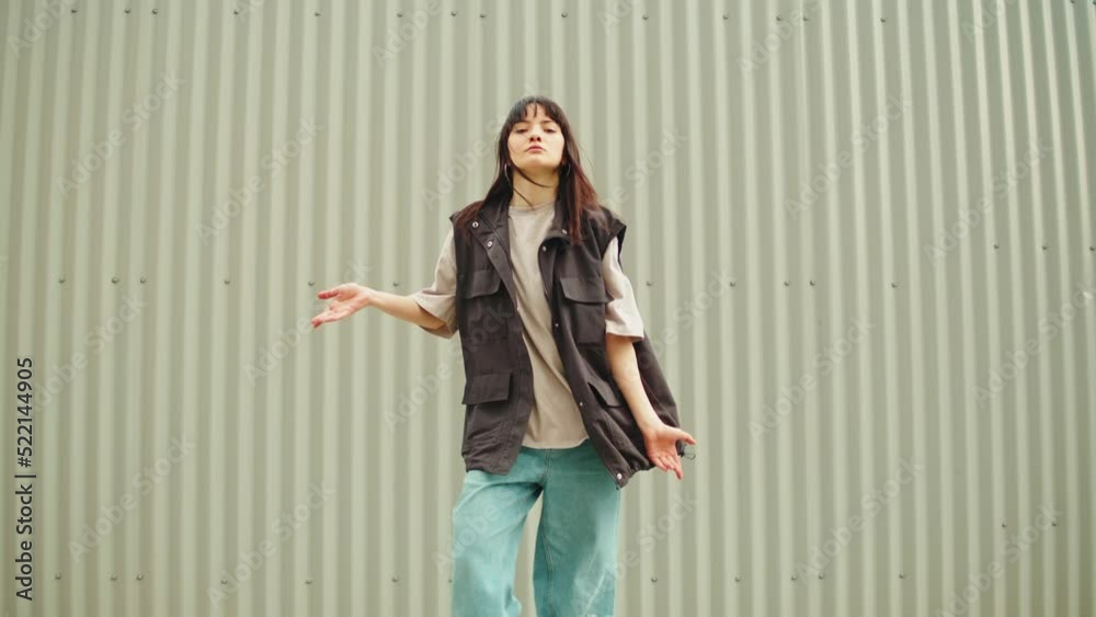 Young woman dancing hip hop. Modern dance choreography. Female professional dancer showing dance movings on striped background wall. Musical video.