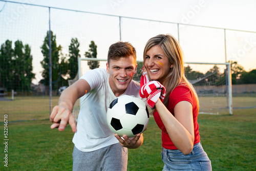 Fototapeta Naklejka Na Ścianę i Meble -  Young beautiful couple of soccer fans holding scarf and soccer ball , pointing at camera