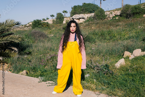 Young girl with long black curly hair wearing yellow jumsuit in nature photo