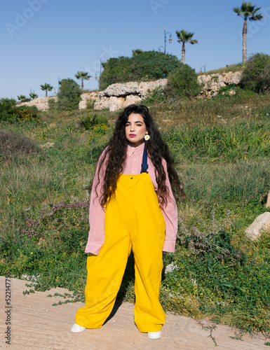 Young girl with long black curly hair wearing yellow jumsuit in nature photo