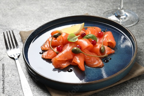 Salmon carpaccio with capers, cranberries, basil and lemon served on grey table