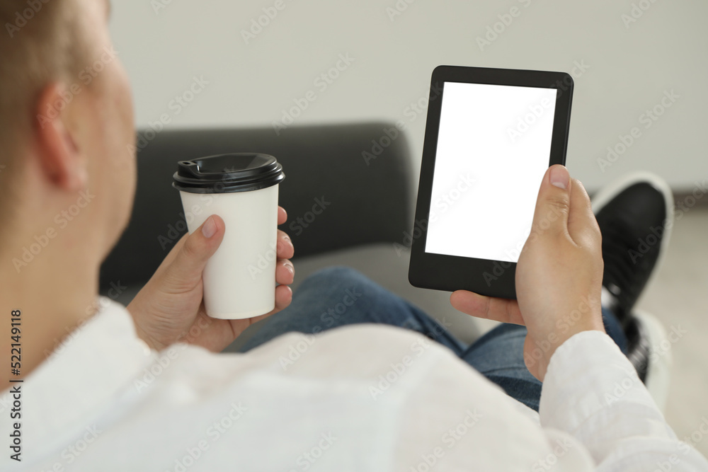 Man with cup of coffee using e-book reader indoors, closeup Man with cup of coffee using e-book reader indoors, closeup