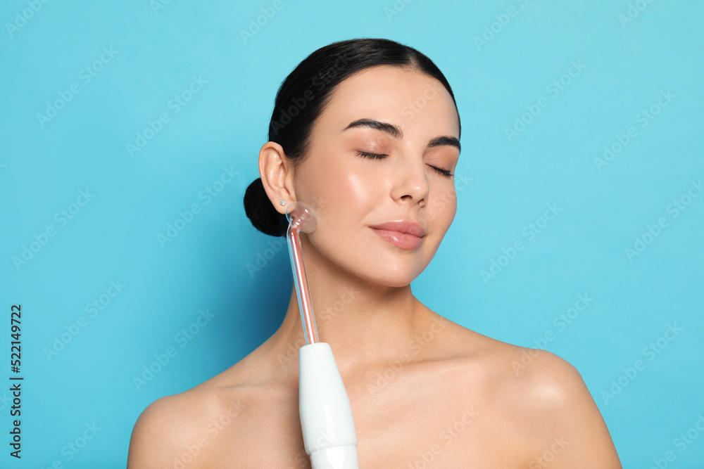 Woman using high frequency darsonval device on light blue background