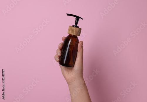 Woman holding bottle of cosmetic product on pink background, closeup
