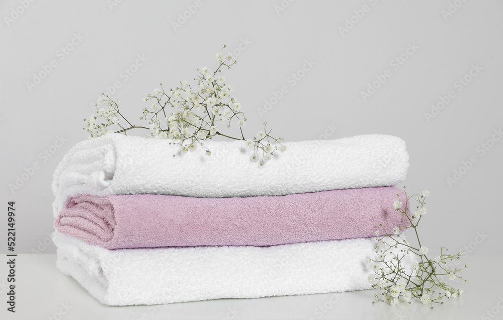 Clean soft towels with flowers on white table against light grey background Clean soft towels with flowers on white table against light grey background