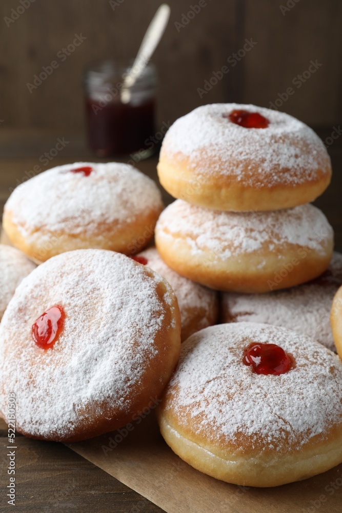 Many delicious donuts with jelly and powdered sugar on wooden table, closeup