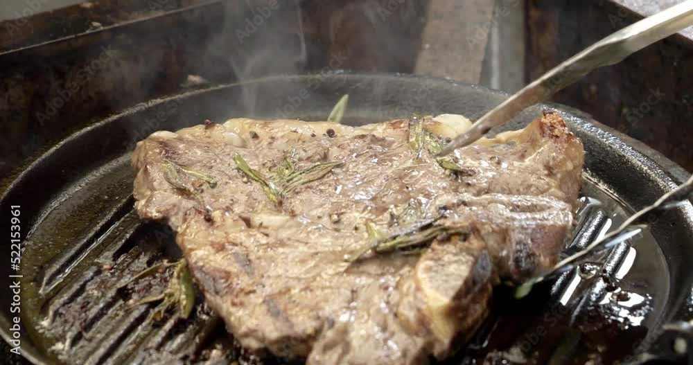 Close up Front view Flipping a Seared Sizzling T-bone Steak in a Grill Pan searing meat, cook in restaurant concept. Close up Front view Flipping a Seared Sizzling T-bone Steak in a Grill Pan searing meat, cook in restaurant concept.