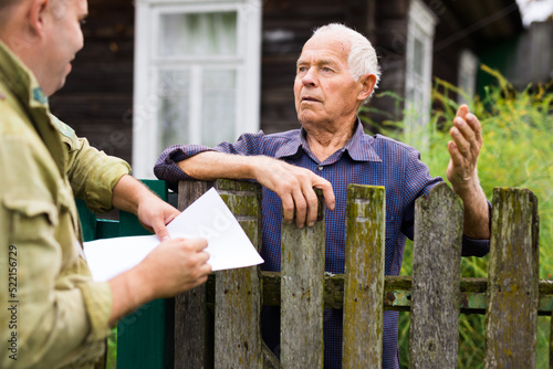 Grandfather talking to census agent standing at fence of his country house photo