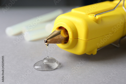 Melted glue dripping out of hot gun nozzle on grey background, closeup photo