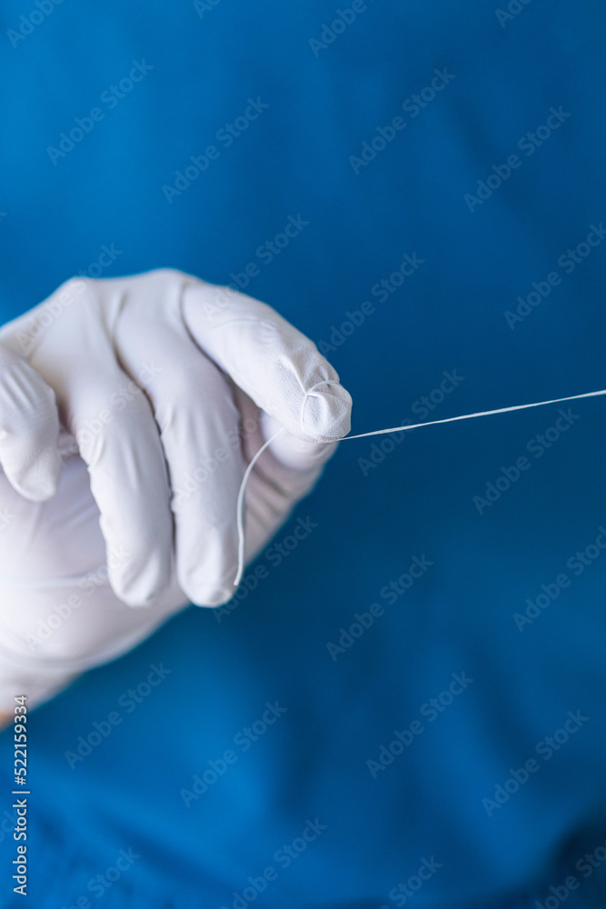 A dentist in gray gloves and blue scrubs holding dental floss A dentist in gray gloves and blue scrubs holding dental floss