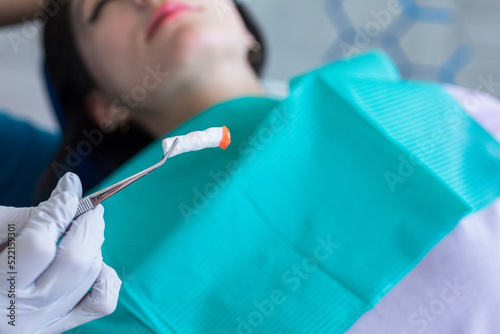 Dentist holding a red anesthetic cotton swab in front of a patient photo