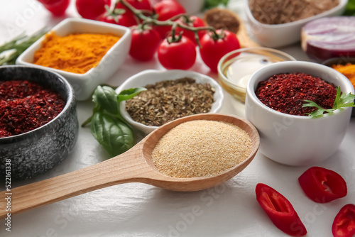 Wooden spoon with dried garlic and different spices on light background