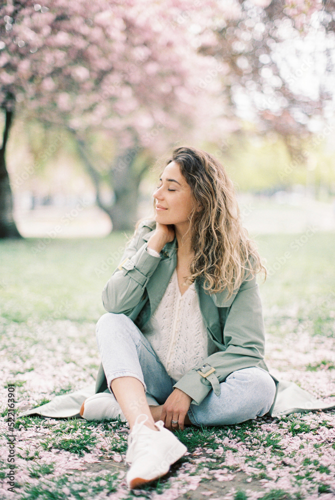 woman sitting on the grass covered with sakura petals woman sitting on the grass covered with sakura petals