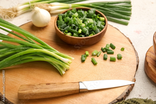 Wooden board with bunch of green onion and knife on table, closeup