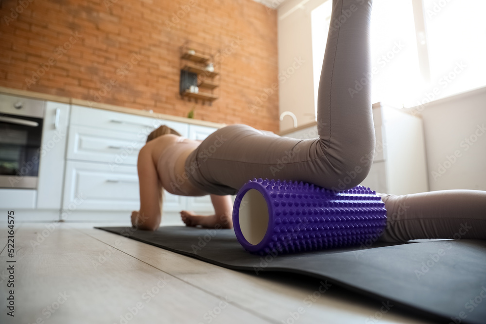 Obraz premium Young woman training with foam roller in kitchen