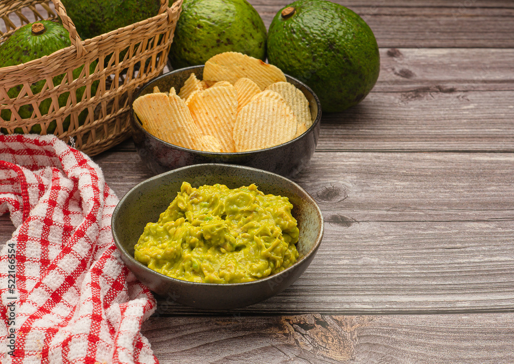 Top view of fresh guacamole in a dish and potato chips on a plate over a wooden table Top view of fresh guacamole in a dish and potato chips on a plate over a wooden table