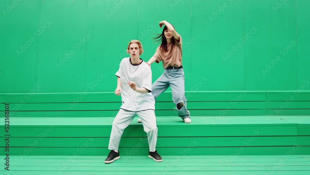 Young couple dancing hip hop on green background wall. Modern dance choreography. Professional dancers man and woman duet showing dance movings. Musical video. Young couple dancing hip hop on green background wall. Modern dance choreography. Professional dancers man and woman duet showing dance movings. Musical video.
