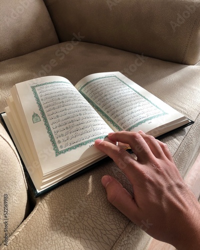 Male hand opening Quran pages on gray armchair photo