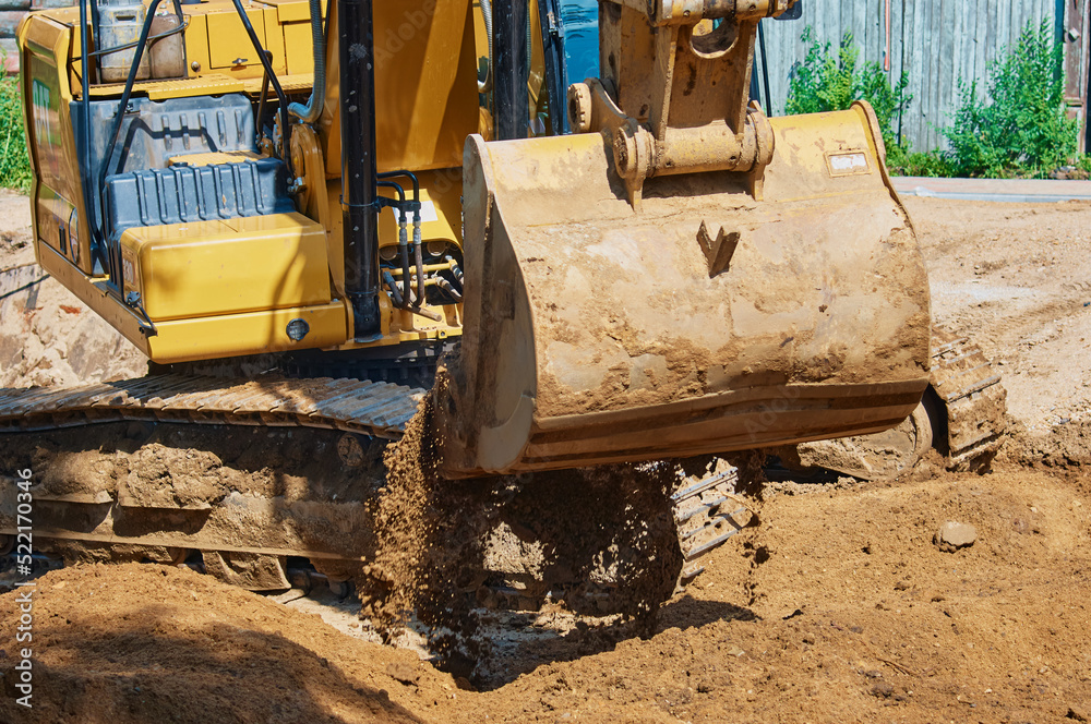 Fototapeta premium Close up view of an excavator bucket full of earth. The process of digging soil at a construction site. Selective focus
