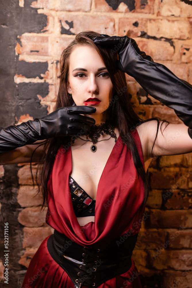 Beautiful girl in a red dress posing. Vampire image. Keeps hands close to face. Halloween concept, nightclub, masquerade Beautiful girl in a red dress posing. Vampire image. Keeps hands close to face. Halloween concept, nightclub, masquerade