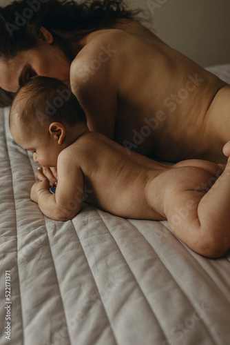 The newborn naked baby is lying on the bed near it's mother at home photo