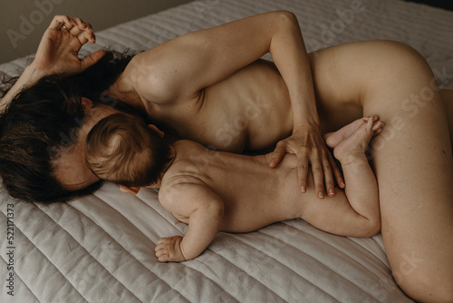 The newborn naked baby is lying on the bed near it's mother at home