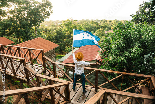 male tourist waving the flag of Honduras in front of some mountain cabins photo