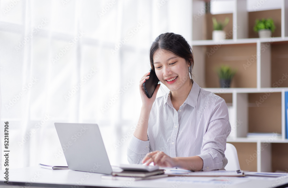 Charming Young business Asian woman manager with a smile working on a laptop holding document and talking on a mobile phone at the office. Charming Young business Asian woman manager with a smile working on a laptop holding document and talking on a mobile phone at the office.